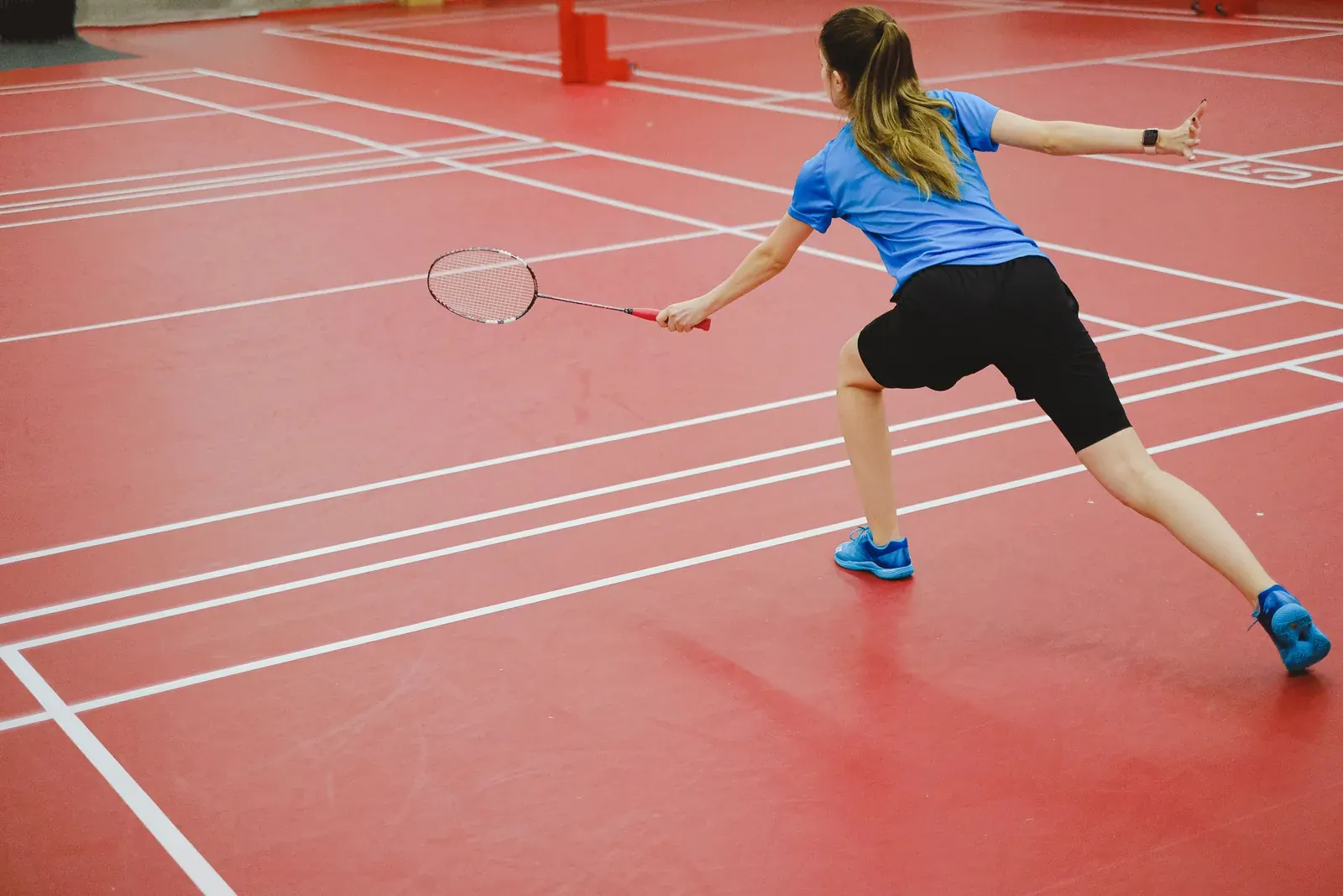 Badminton player lunging for a shot on a red court
