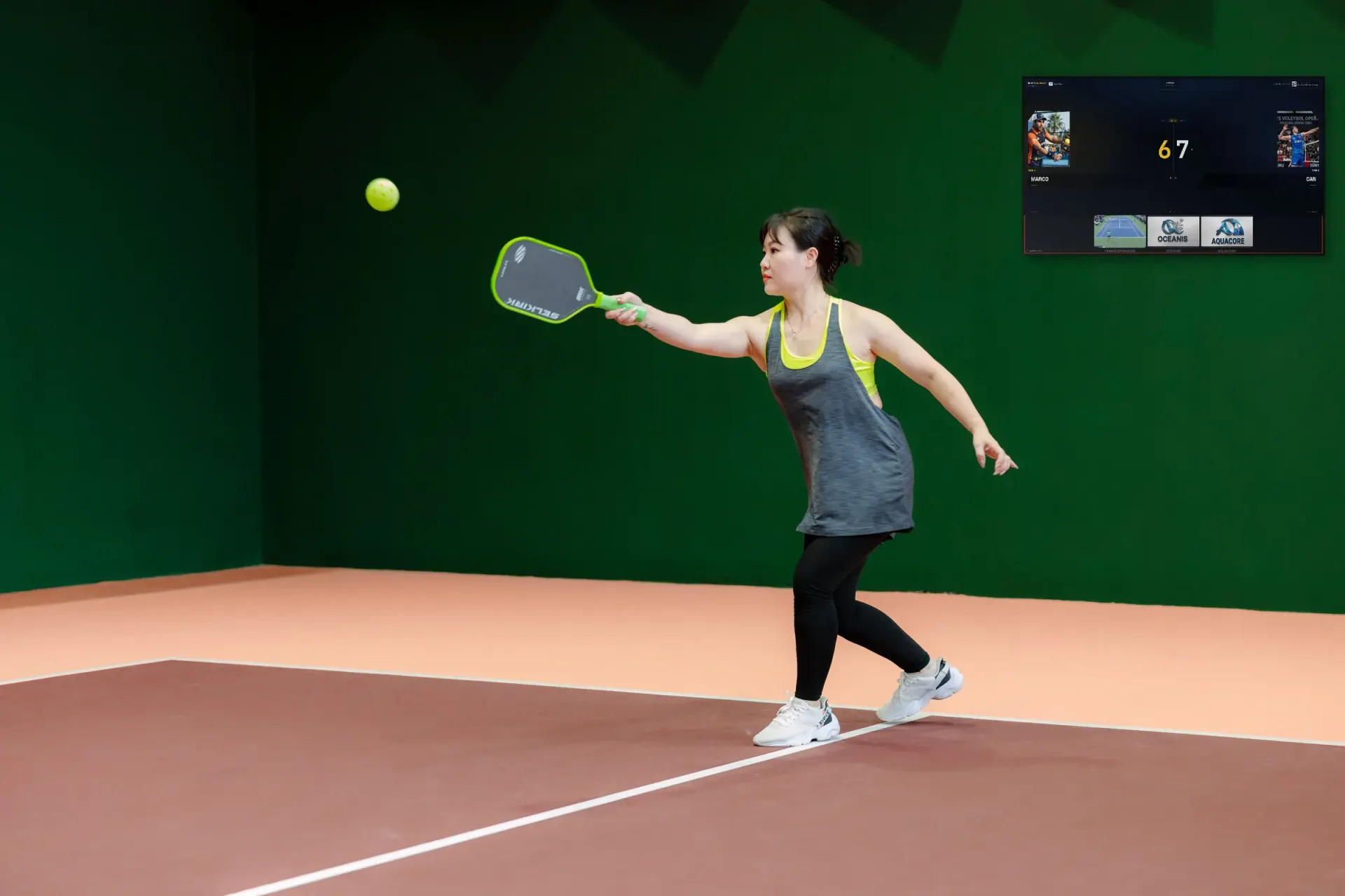 Pickleball player hitting a forehand with a Multi Score Screen scoreboard on the wall