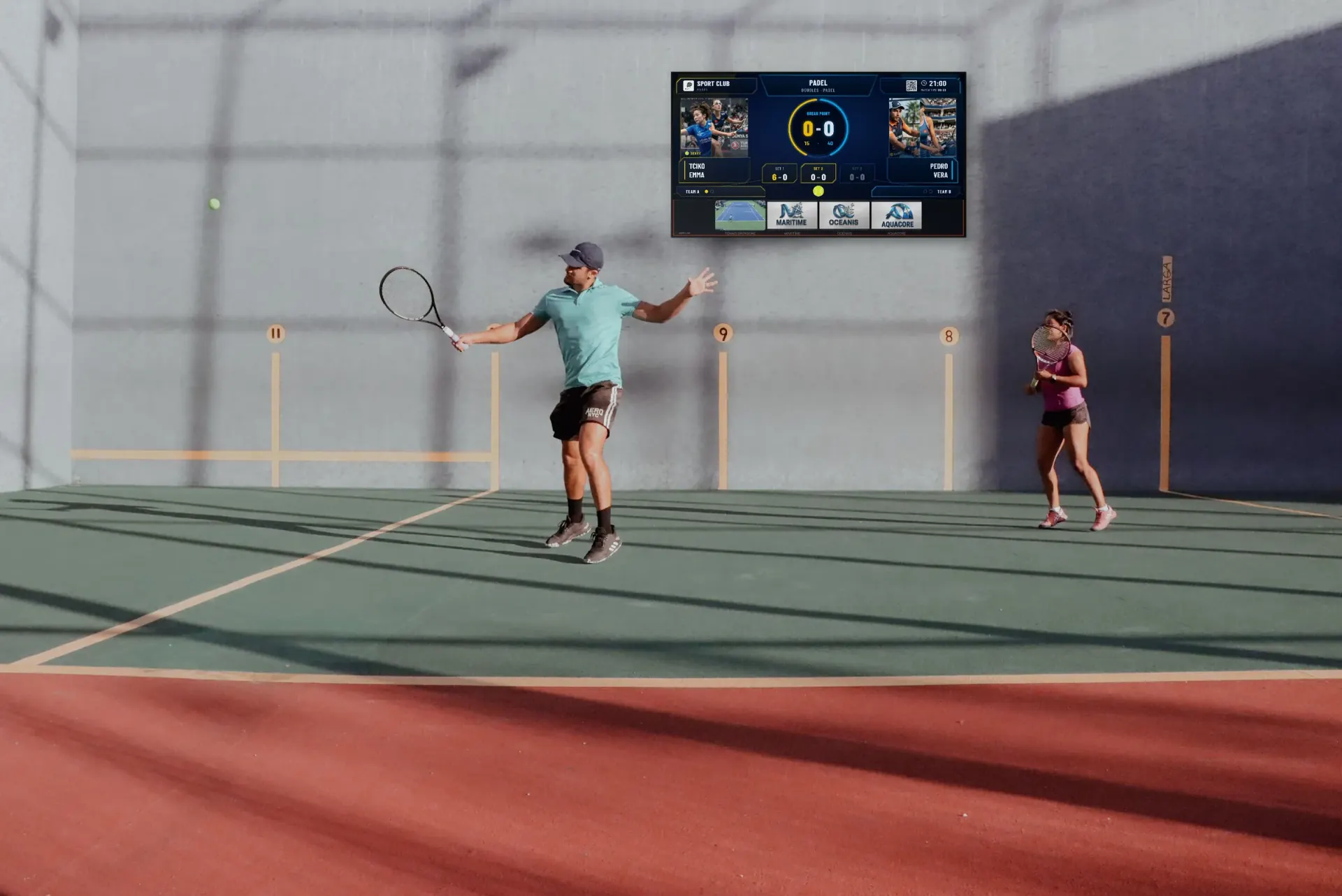 Two players on an outdoor wall court with a Multi Score Screen scoreboard on the wall