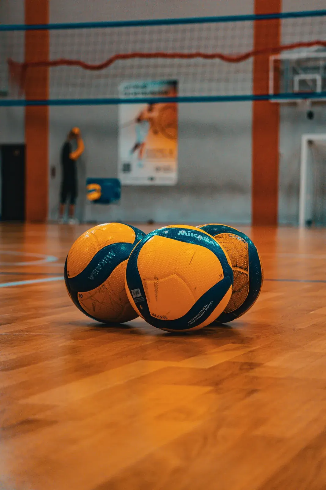 Tres balones de voleibol sobre el suelo de madera de un pabellón